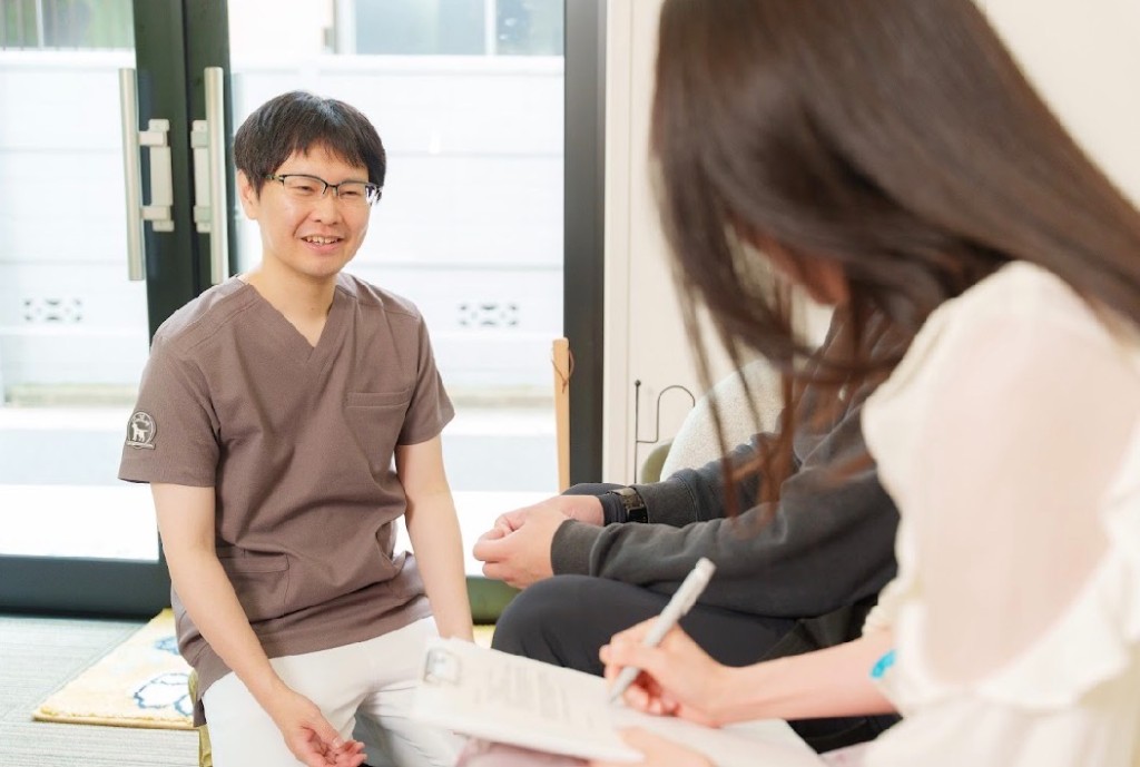 施術者がカップルと向き合い説明する様子。女性がメモを取りながら聞いている。二人三脚の妊活のイメージ。