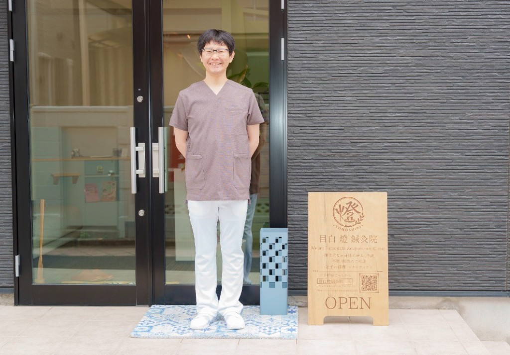院長のポートレート。医院の入口前で、スクラブ姿で微笑んでいる様子。